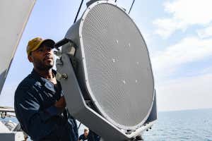 Marinero de la Armada de EE. UU. Utiliza audífonos de largo alcance a bordo de un barco